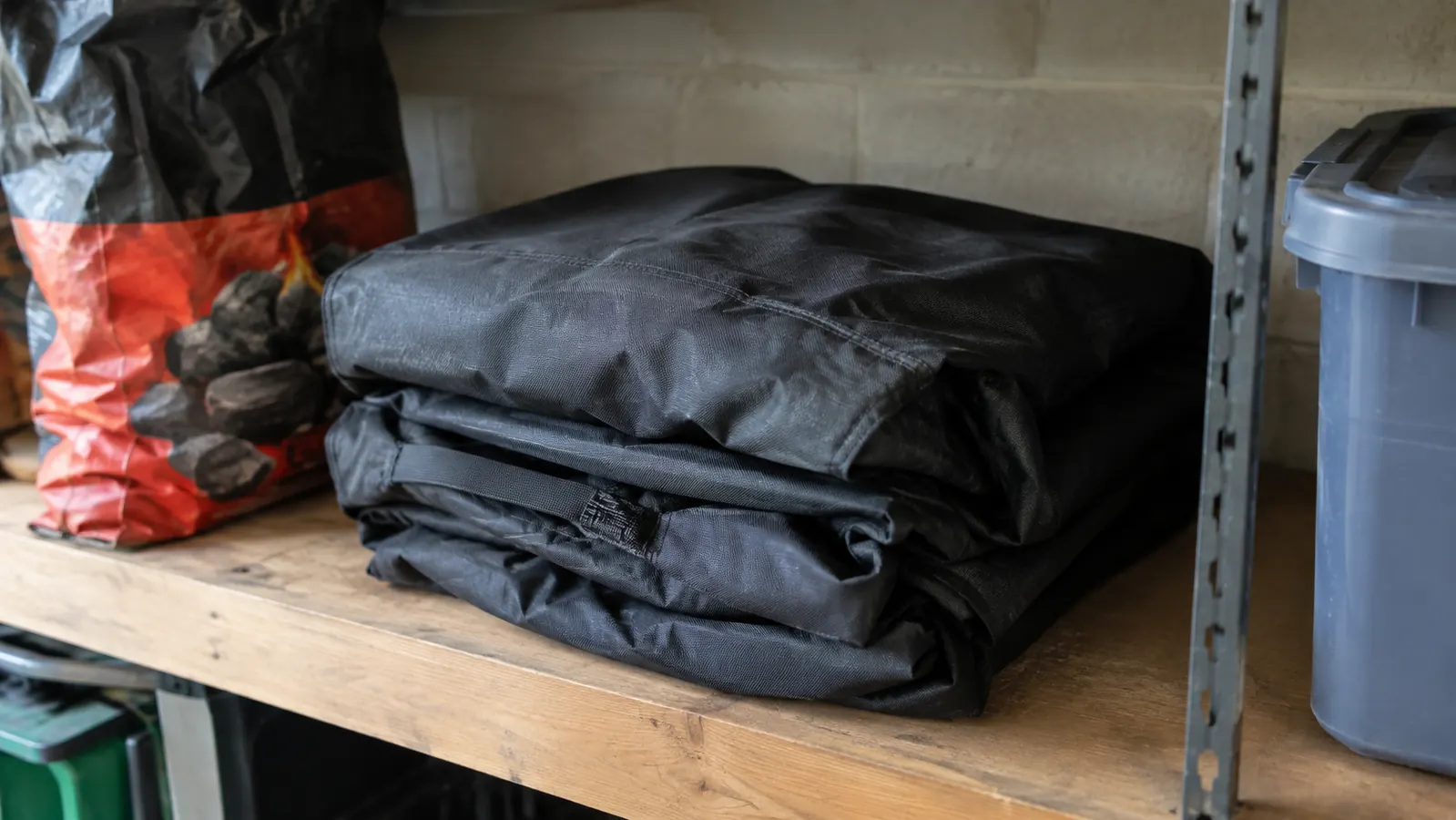 A folded grill cover on a garage shelf next to a bag of charcoal