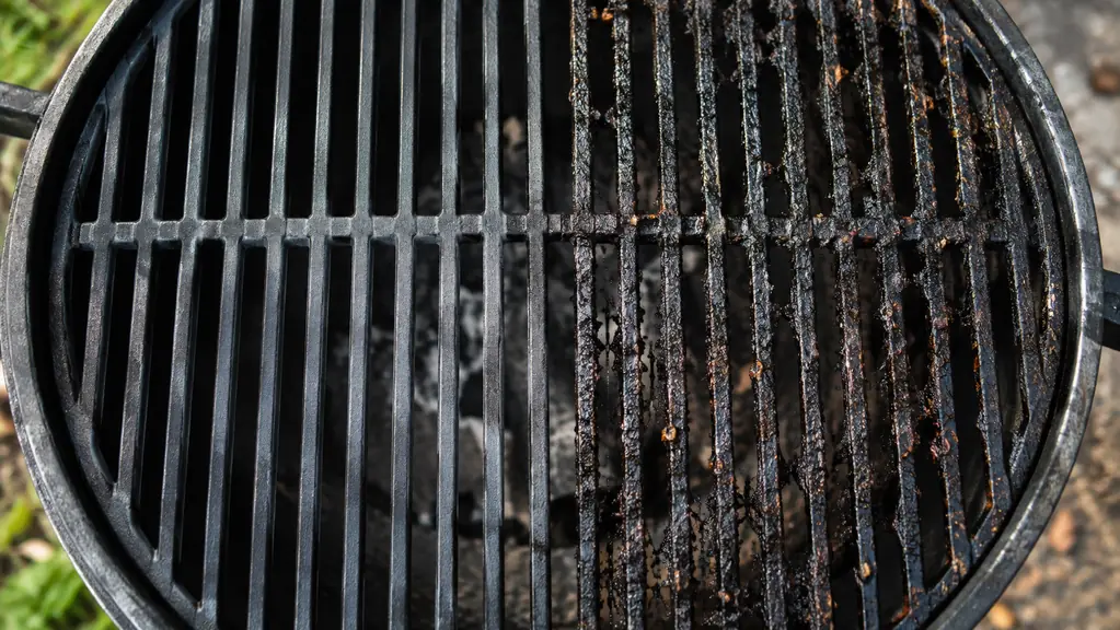 Close view of a cast iron grill grate half cleaned and half still covered in carbon